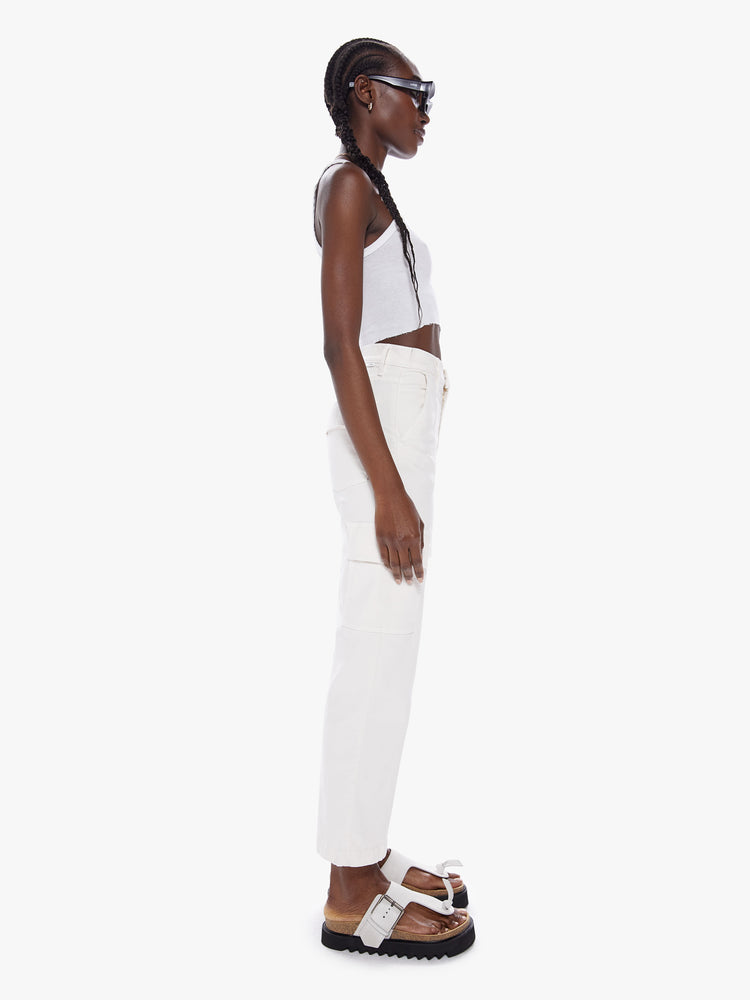 Side view of a woman High-waisted ankle-length pants with a wide straight leg, cargo pockets and seams down the front in an off white hue.