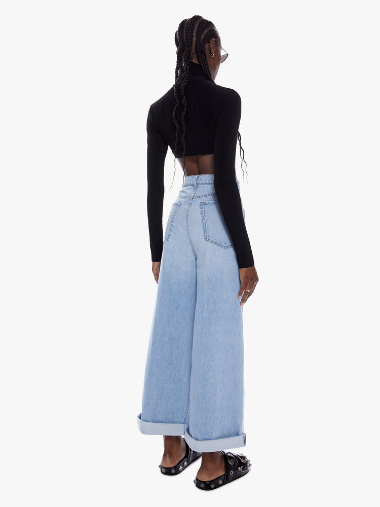 Back full body view of a woman in super wide leg from SNACKS MOTHERS throwback styles of 80s and 90s a high rise jean with a cropped inseam a cuffed hem and a loose roomy fit in a faded light blue wash