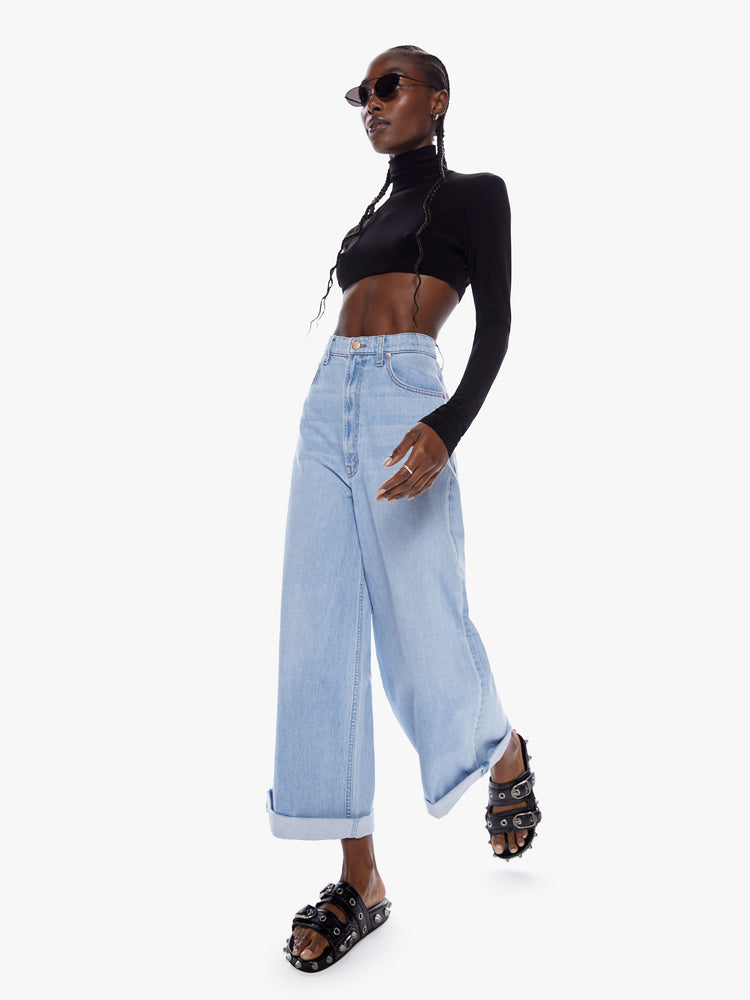 In motion full body view of a woman in super wide leg from SNACKS MOTHERS throwback styles of 80s and 90s a high rise jean with a cropped inseam a cuffed hem and a loose roomy fit in a faded light blue wash