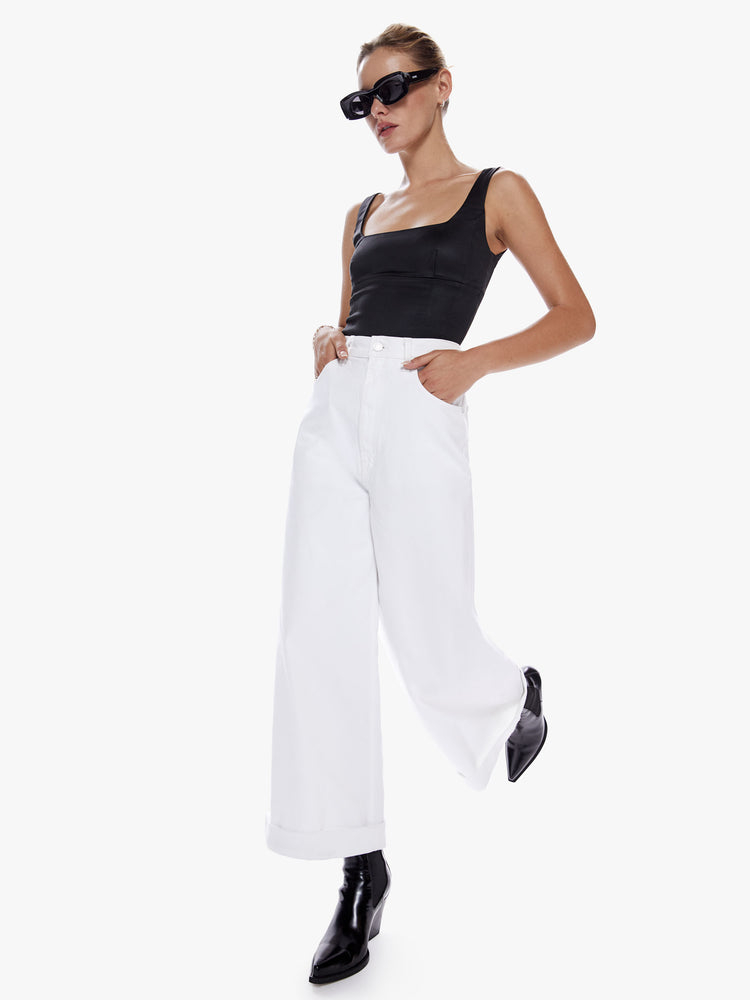 Front in motion full body view of a woman in a super wide leg jean from snacks, mother's homage to throwback styles of  80 and 90s, the high rise jean features a cropped inseam with a cuffed hem and loose, roomy fit in a clean white hue