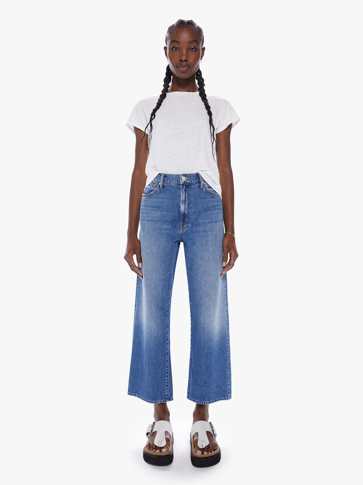 Front full body view of woman in a high waisted jean with loose wide leg and an ankle length inseam cut from a recycled cotton blend denim in a midblue wash with whiskering and fading at the knees