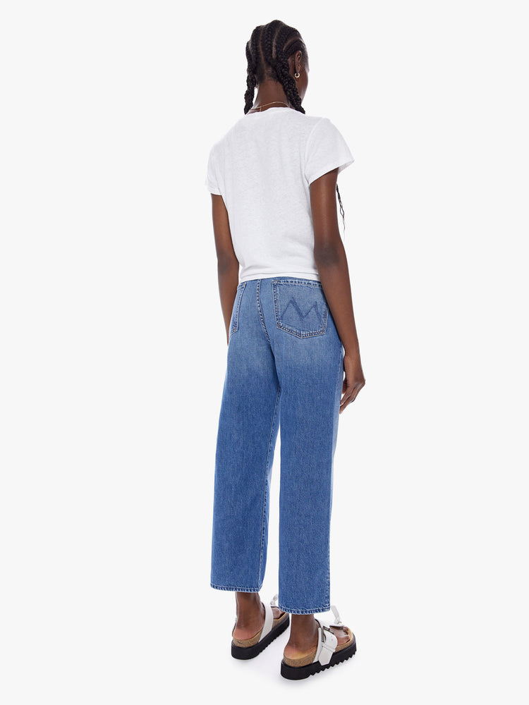 Back full body view of woman in a high waisted jean with loose wide leg and an ankle length inseam cut from a recycled cotton blend denim in a midblue wash with whiskering and fading at the knees