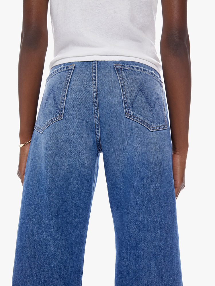 Close back view of woman in a high waisted jean with loose wide leg and an ankle length inseam cut from a recycled cotton blend denim in a midblue wash with whiskering and fading at the knees