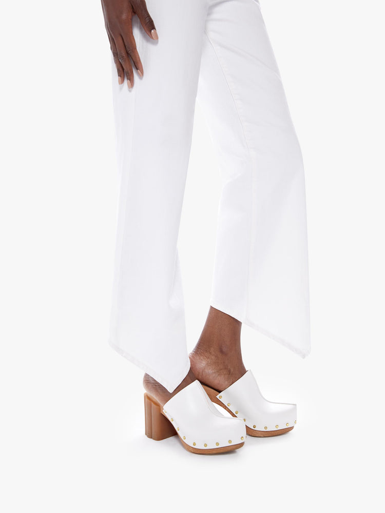 Hem close up view of a woman in a high waisted straight leg jeans with a vshaped front hem and a shorter hem in the back cut from semi-rigid superior denim, in a classic white hue with tonal hardware