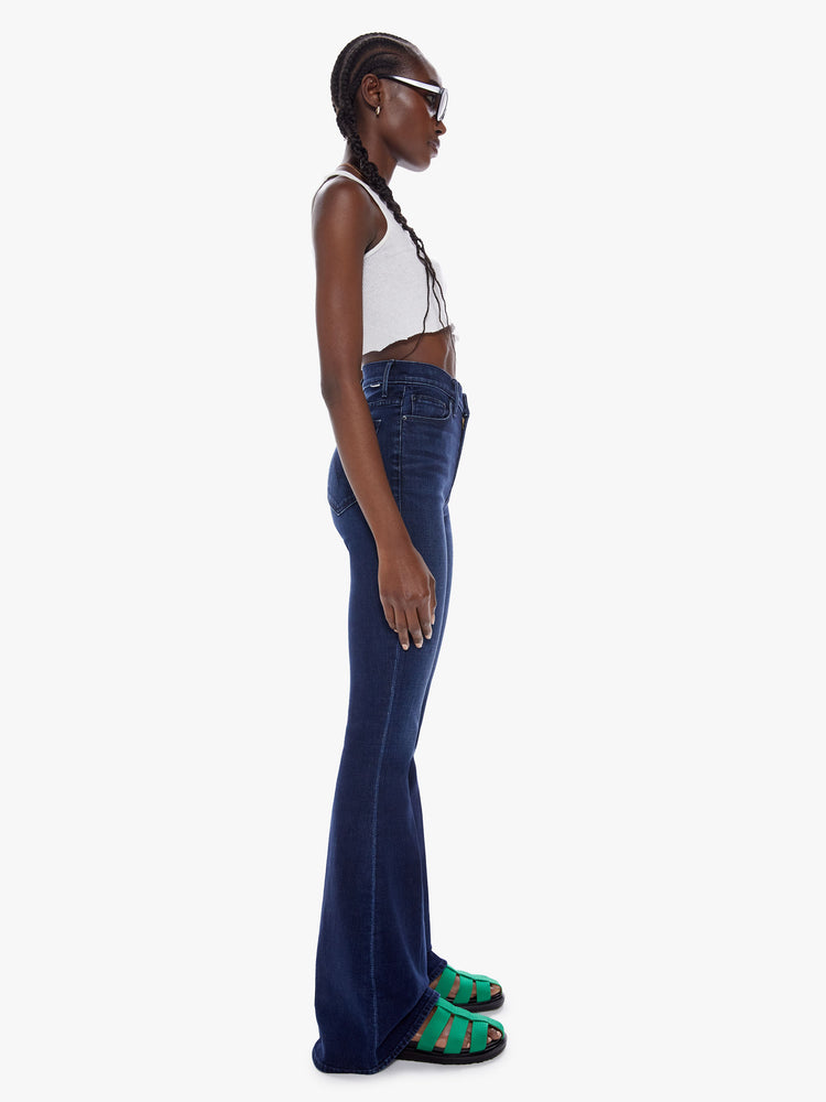 Side view of woman high-rise flare with a long 34.5-inch inseam and a clean hem in a dark blue wash.