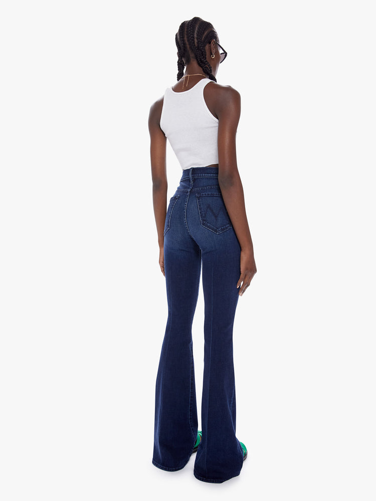 Back view of woman high-rise flare with a long 34.5-inch inseam and a clean hem in a dark blue wash.