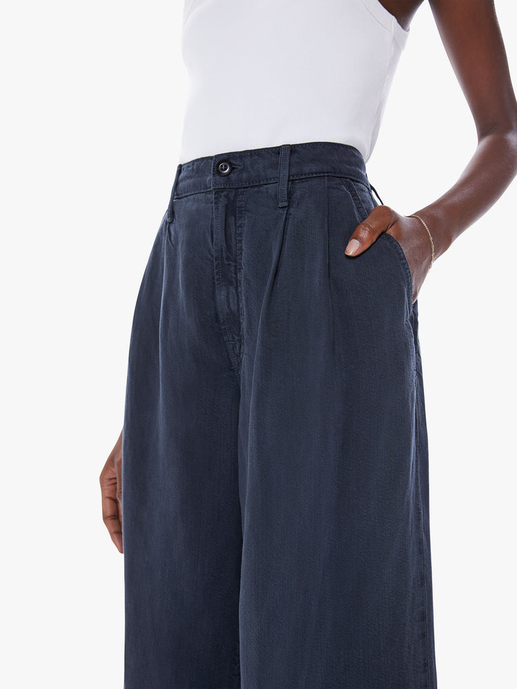 Close up view of womans high-waisted wide leg pant with a pleated waistband, back slit pockets, an ankle-length inseam and a clean, thick hem in a faded black hue.
