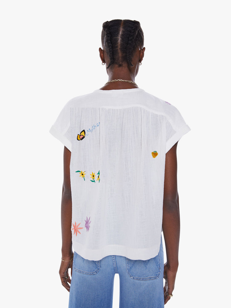Back view of woman's blouse with a buttoned V-neck, rolled short sleeves, gathered seams at the shoulders and a boxy fit in semi-sheer white with embroidered flowers, mushrooms and butterflies.