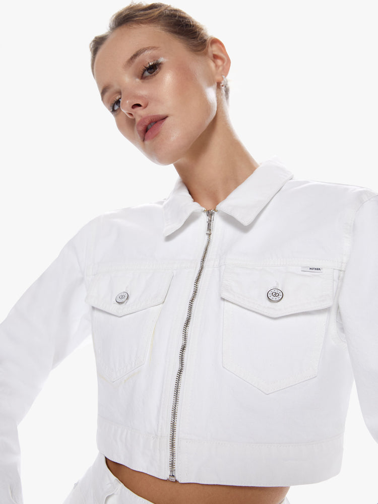 Close up view of a woman in a denim jacket from snacks mothers homage to throwback styles of the 80s and 90s, the zip up jacket features front patch pockets, long sleeves and cropped hem with a slightly boxy fit in a white hue