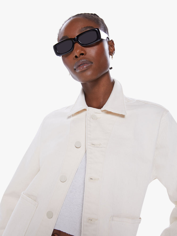 Close up view of women's denim jacket with oversized front patch pockets, cropped long sleeves and a boxy fit in a creamy white hue.
