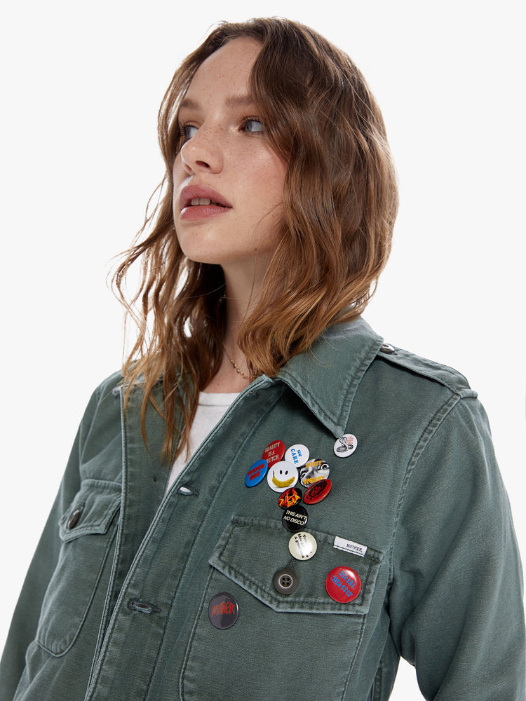 Close up front view of a woman in a military inspired jacket with a front patch pockets and a cropped, fray hem made from 100% cotton deadstock fabric, Roger That is a classic army green hue with tonal buttons and decorative pins on the chest