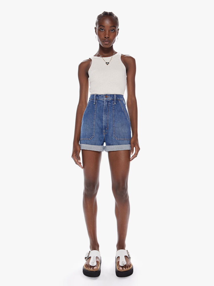 Front full body view of a woman in an ultra high waisted shorts with oversized patch pockets, a short 3-inch inseam and a rolled hem in a mid-blue wash with subtle fading throughout