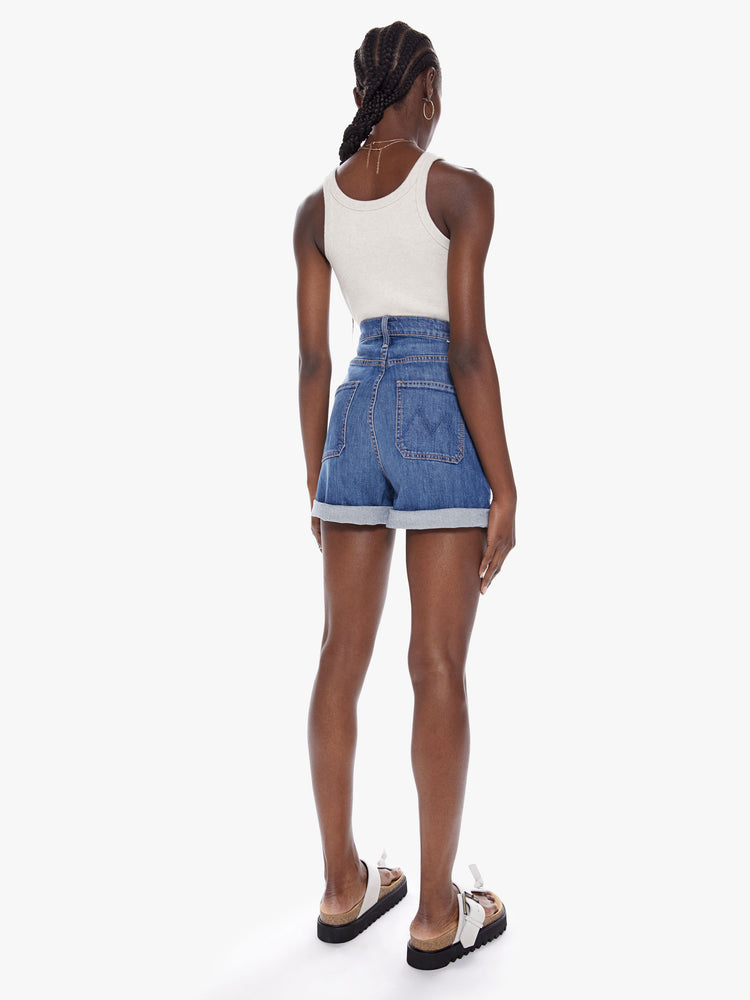 Back full body view of a woman in an ultra high waisted shorts with oversized patch pockets, a short 3-inch inseam and a rolled hem in a mid-blue wash with subtle fading throughout