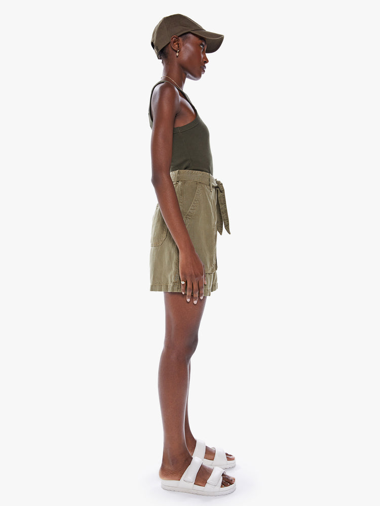 Side view of a woman High-waisted paperbag shorts with a tied waist, oversized patch pockets in an olive green hue with faded details.