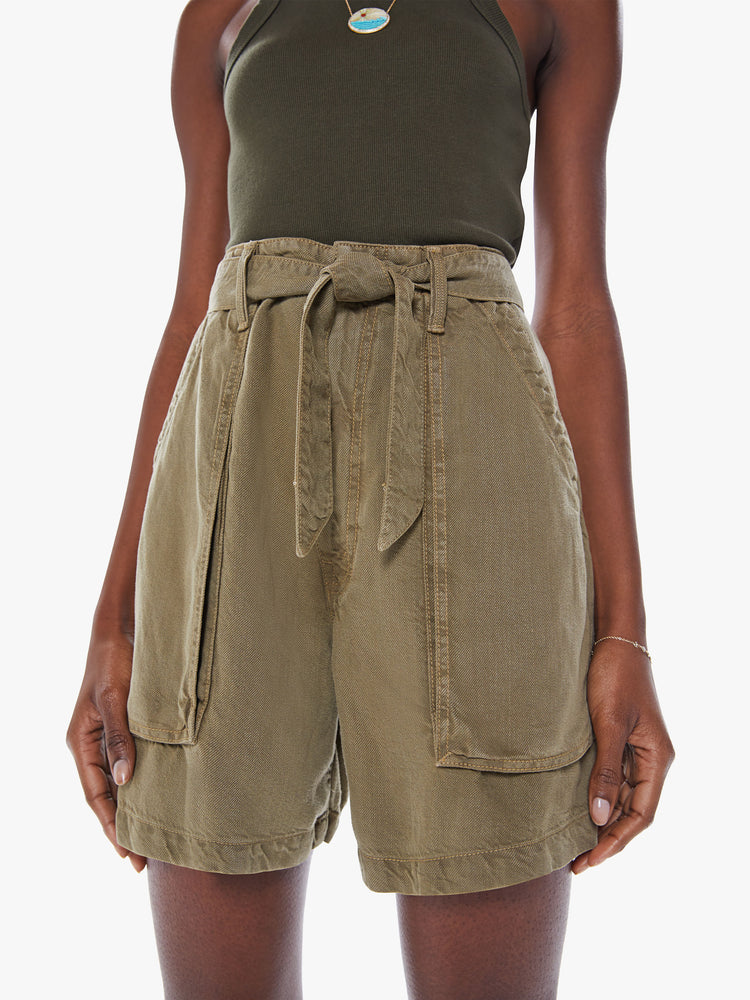 Close up view of a woman High-waisted paperbag shorts with a tied waist, oversized patch pockets in an olive green hue with faded details.