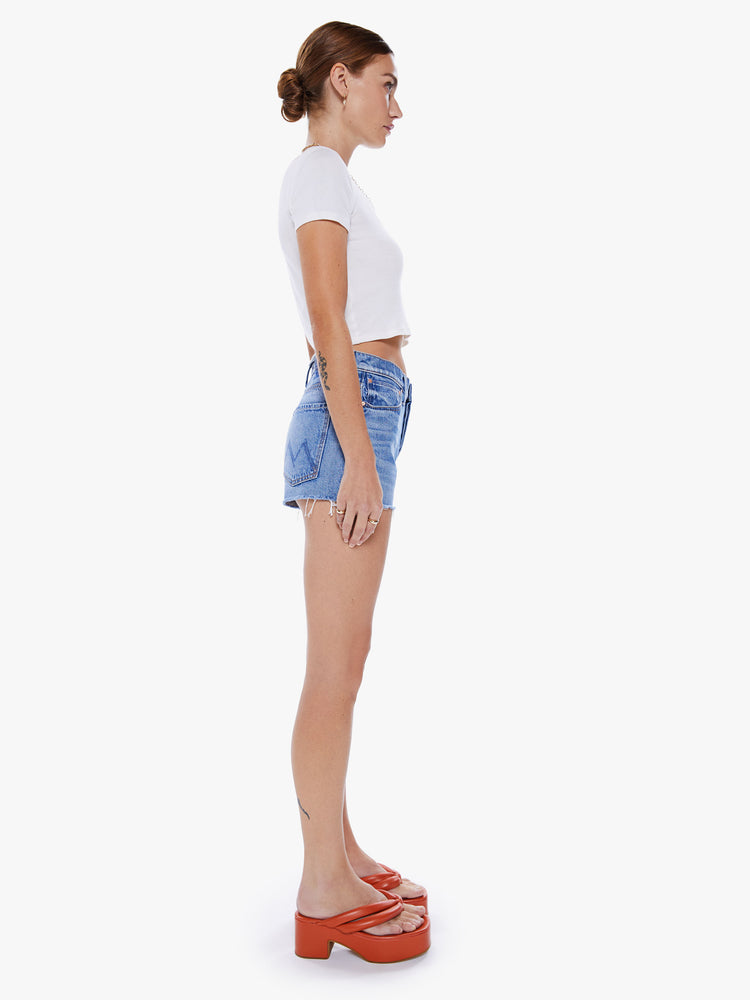 Side view of a woman denim short with button fly, 1 inch inseam, frayed hem and relaxed fit in a mid blue wash.