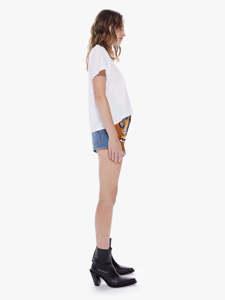 Side full body view of a woman in a high waisted denim short with a short inseam, raw hem, and a faux-suede panel on the front with fridge cut from semi-rigid superior denim in a mid-blue wash detailed with crochet applique on the front and back