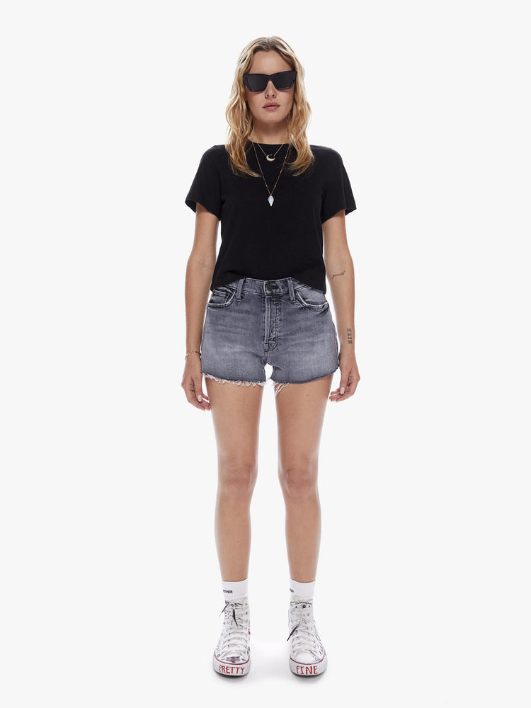 Front view of a woman in a highwaisted jean short with a button fly and a frayed hem made from semi rigid superior denim in a faded black with a subtle distressing for a worn in look