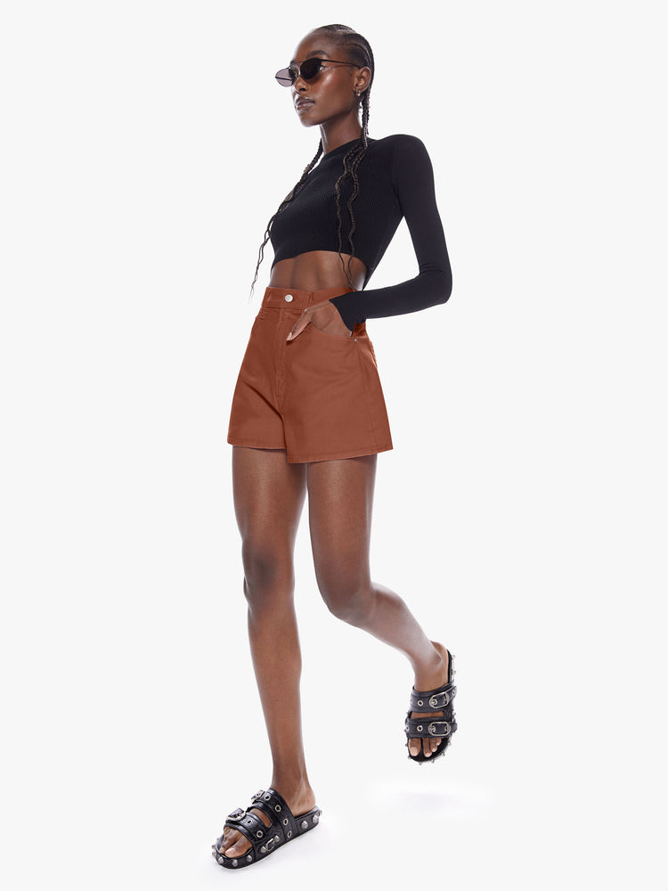 In motion full body view of a woman in denim shorts from SNACKS from mothers homage to throwback styles of the 80s and 90s, the high rise shorts are designed with a super short inseam and a loose wide fit in a dark khaki hue