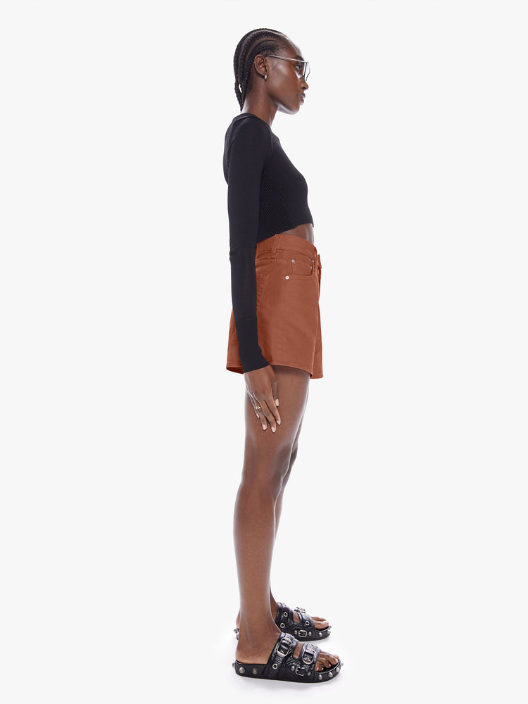 Side full body view of a woman in denim shorts from SNACKS from mothers homage to throwback styles of the 80s and 90s, the high rise shorts are designed with a super short inseam and a loose wide fit in a dark khaki hue