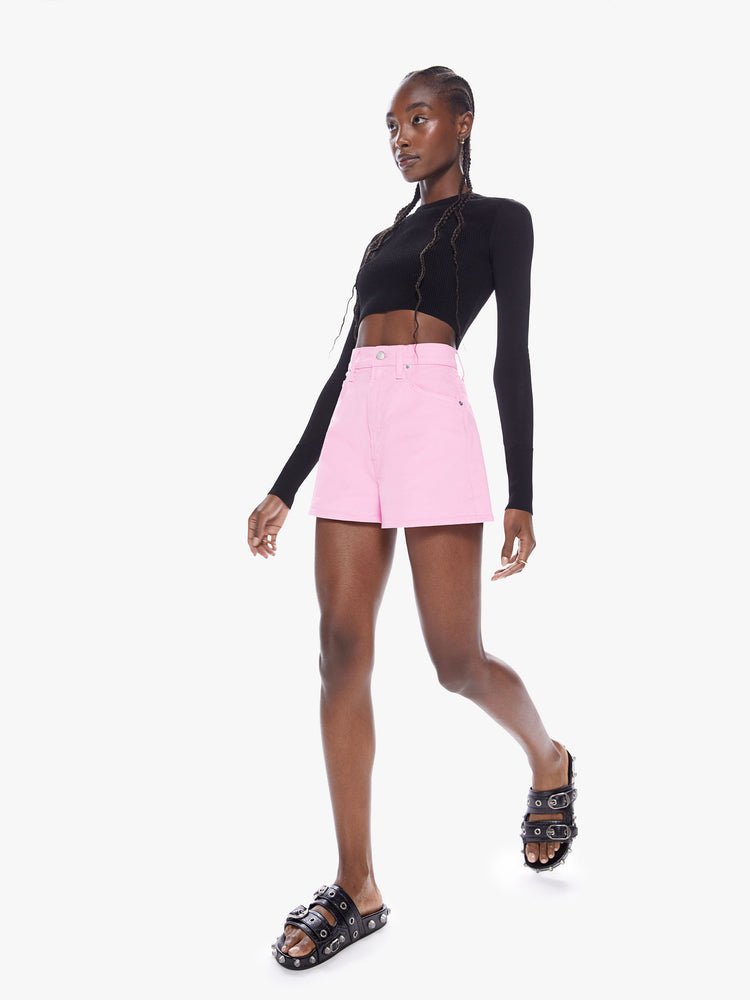 Front in motion full body view of a woman in denim shorts from SNACKS from mothers homage to throwback styles of the 80s and 90s, the high rise shorts are designed with a super short inseam and a loose wide fit in a baby pink hue