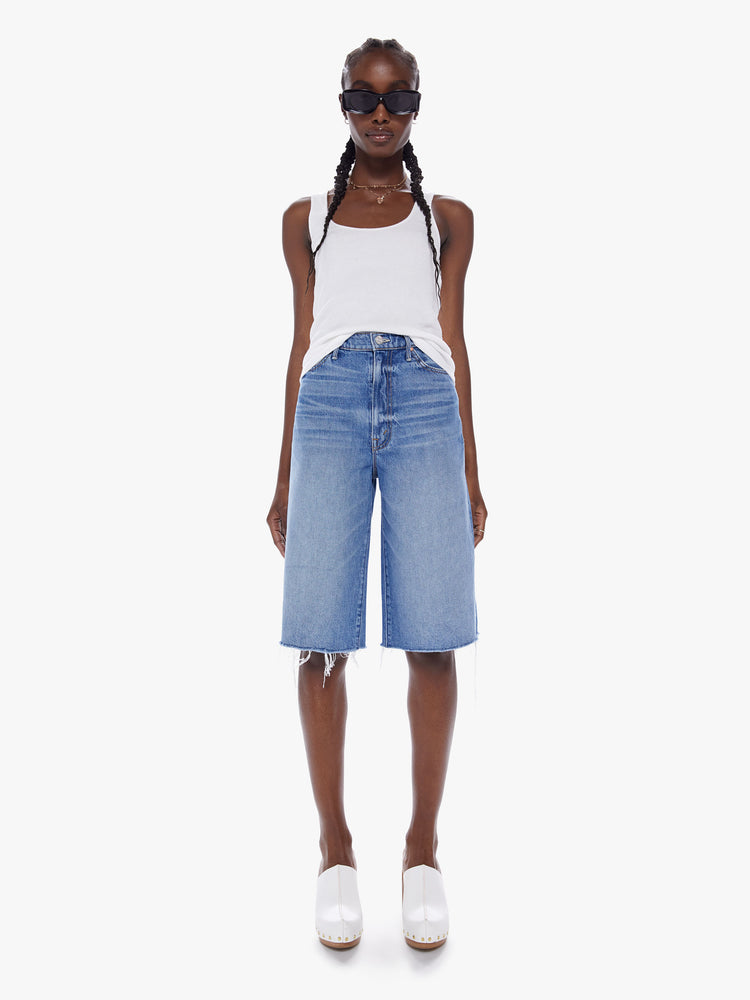 Front view of a woman knee-length shorts feature a high rise, wide leg and frayed hem in a mid blue wash. 