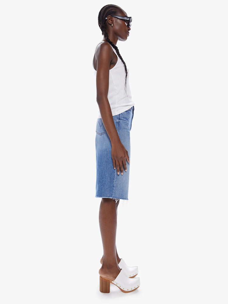 Side view of a woman knee-length shorts feature a high rise, wide leg and frayed hem in a mid blue wash.