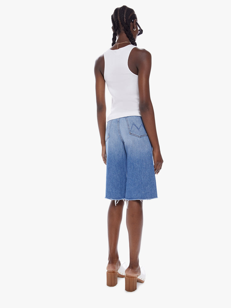 Back view of a woman knee-length shorts feature a high rise, wide leg and frayed hem in a mid blue wash.