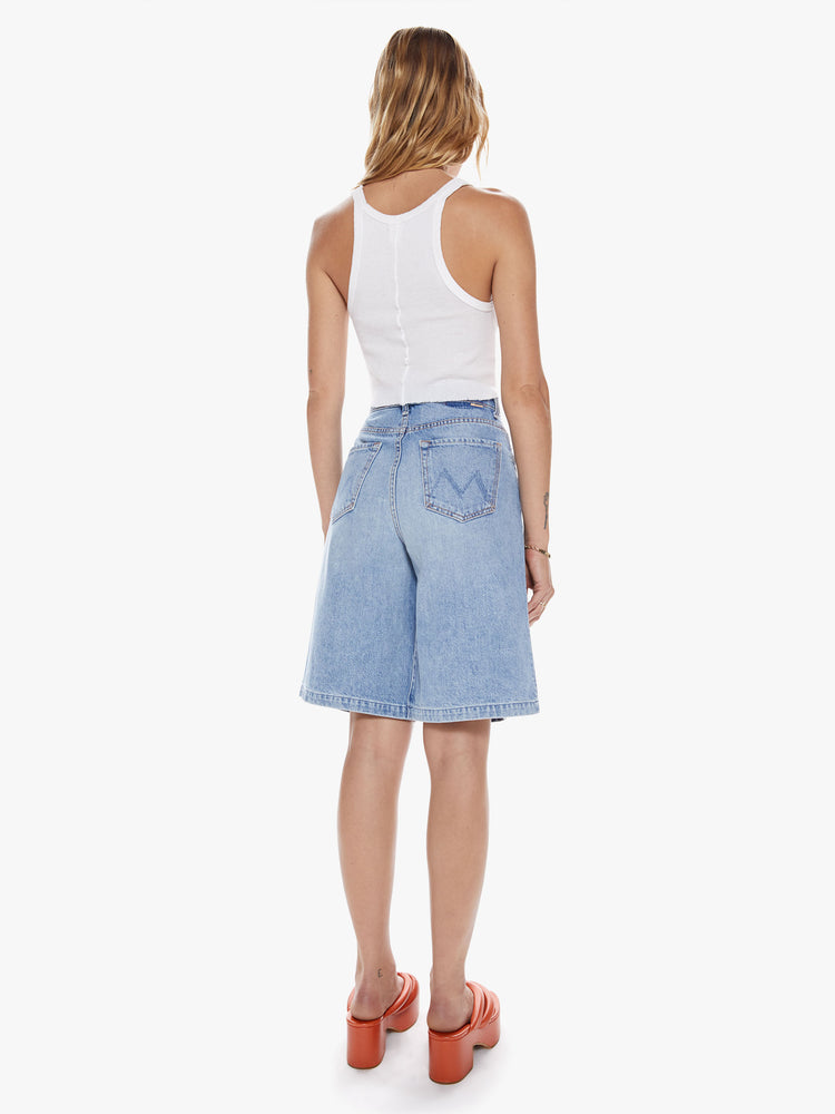 Back full body view of a woman in a bermuda short features a high rise, knee-length hem and a wide leg with pleats at the waist for an even roomier fit in a light blue wash with fading throughout
