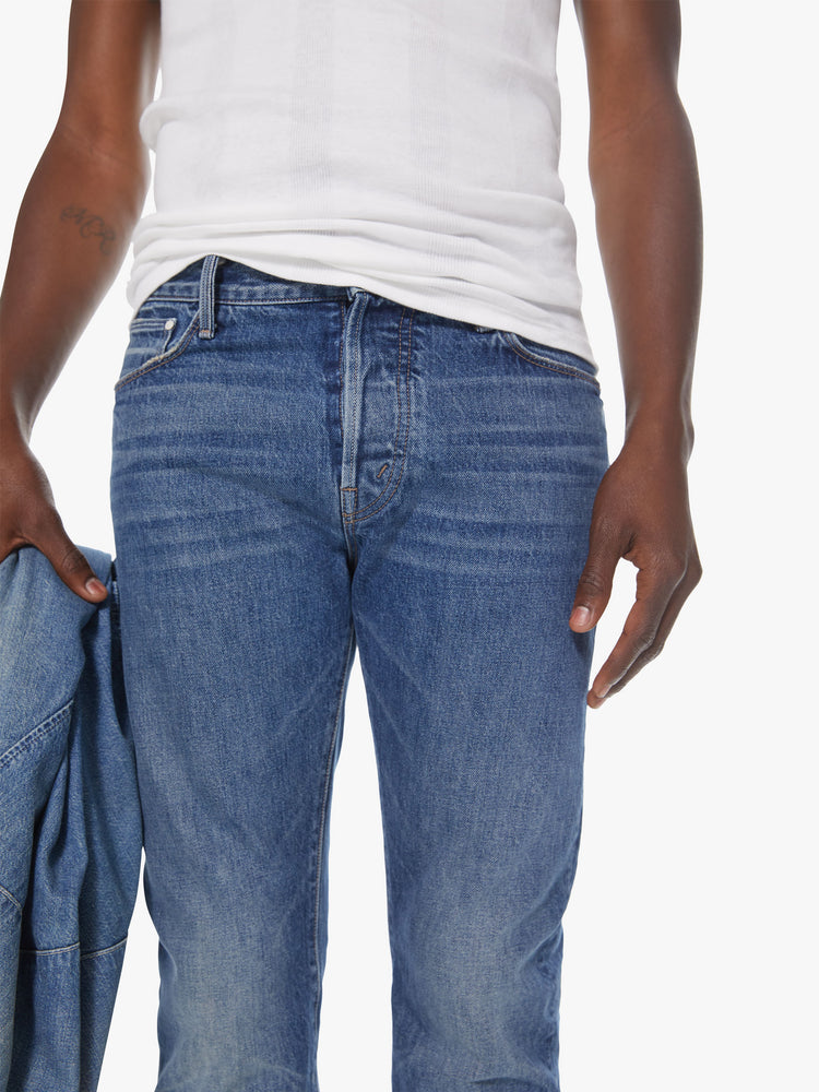 Front detail view of a men's medium blue straight leg jean with fading and whiskers