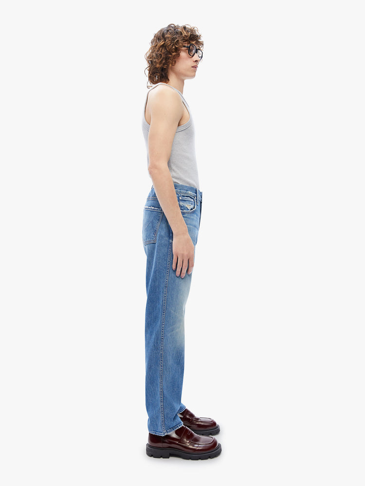 Side view of a men's straight-leg jean with a mid rise, ankle-length inseam and a clean hem in a mid blue wash with subtle whiskering,fading and distressed details