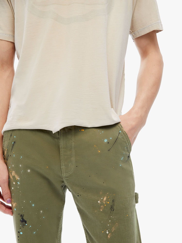Front close up view of a mens classic pant with utilitarian pockets, a hammer loop and relaxed leg in an army green hue with paint splatters and tonal hardware.