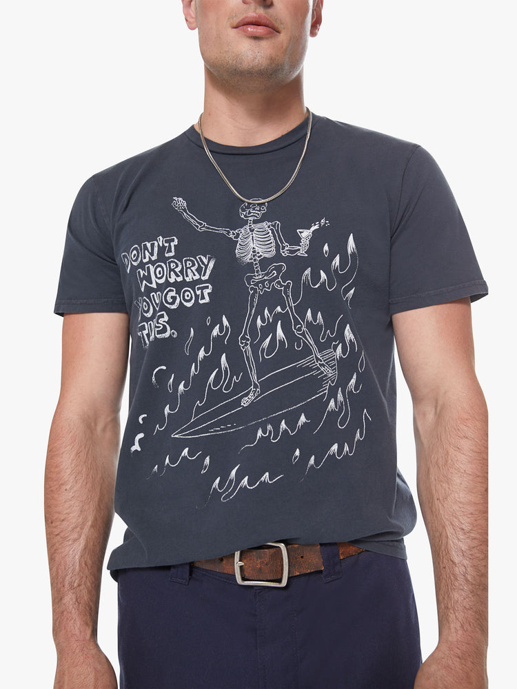 Front detail view of a men's charcoal t-shirt with a white graphic of a skeleton riding a surfboard through flames with "Don't worry you got this" printed in boxy font