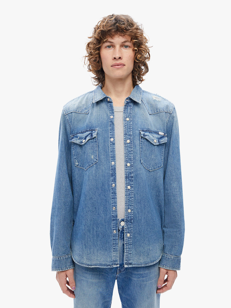 Front view of a mens classic Western-inspired shirt with snap buttons, flap patch pockets, long sleeves and a curved hem in a a mid-blue wash with fading at the shoulders for a worn-in look