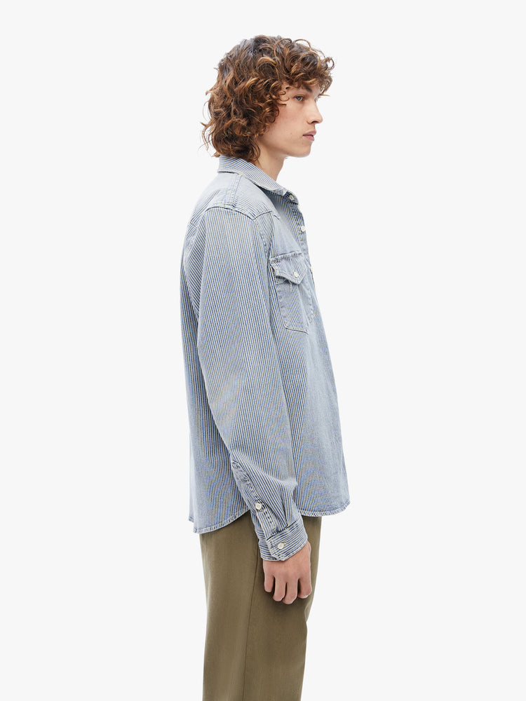 Side view of a mens classic Western-inspired shirt with snap buttons, flap patch pockets, long sleeves and a curved hem in a light-blue wash with navy pinstripes.