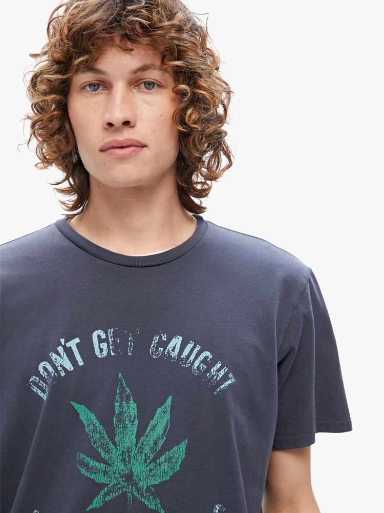 Close up view of a mens classic crewneck tee with short sleeves and a boxy fit, n black, the tee features a faded weed leaf graphic and some advice from MOTHER on the front.