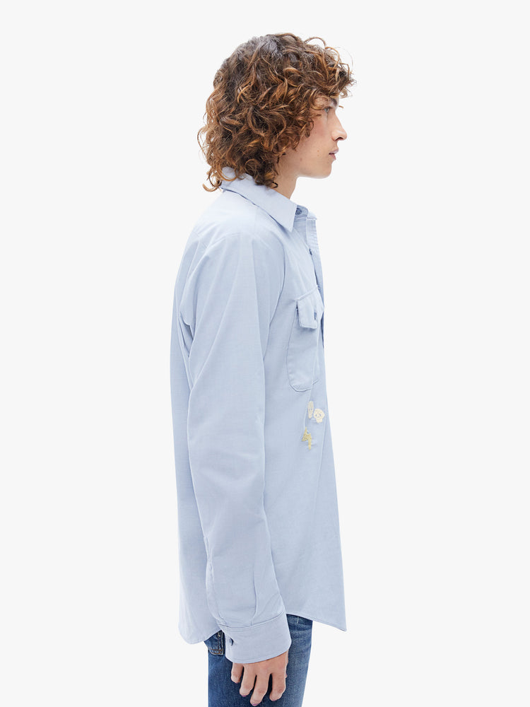 Side view of a mens long-sleeve button-up with front patch pockets and a curved hem in a light blue hue with embroidered details on the front and back.