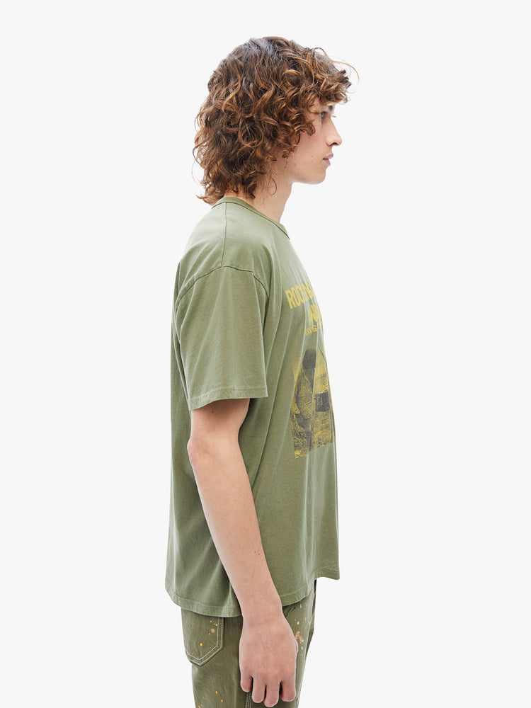 Side view of a mens oversized tee with drop shoulders and a loose fit made from 100% supima cotton in an army-green hue featuring yellow 70s-inspired graphic on the front.