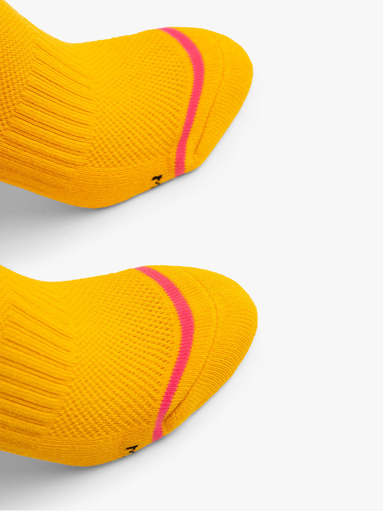 Close up view of a pair of deep yellow socks with dark pink stripes and the words "MAGIC" and "HOUR".