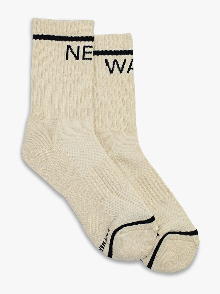 Top flat view of a pair of off white socks featuring black stripes and the words "NEW" "WAVE".