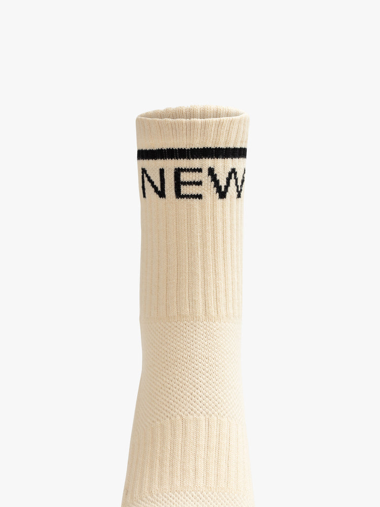 Front close up view of an off white sock featuring a black stripe around the ankle and the word "NEW".