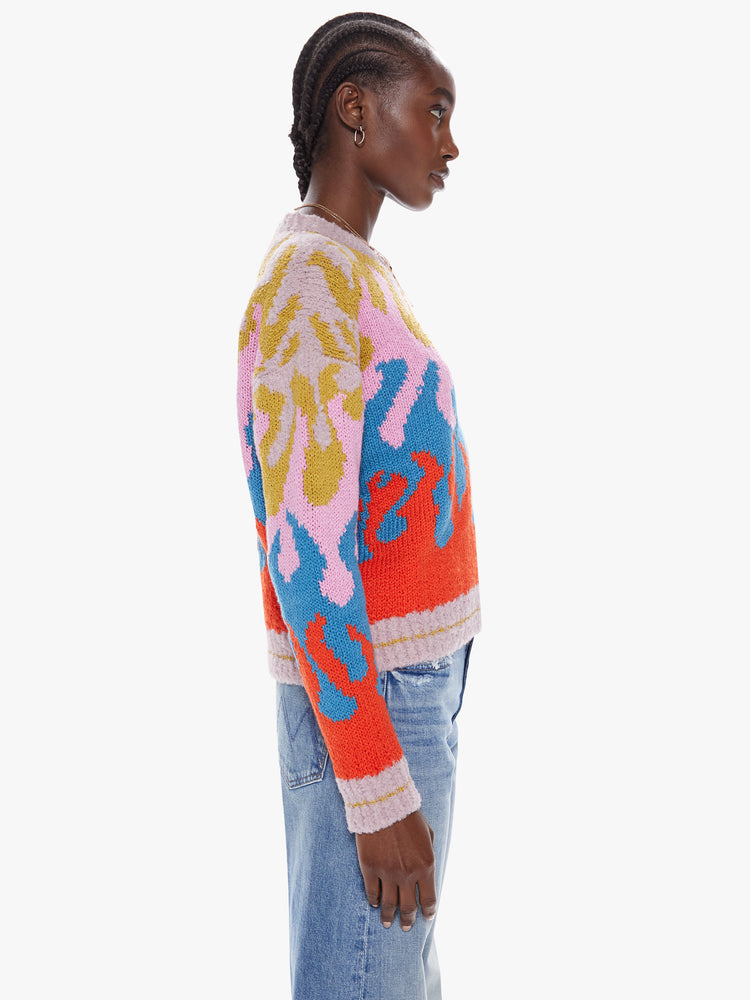 Side view of a womens slightly cropped with long roomy sleeves crewneck sweater with a colorful flame design and stripes at the hem
