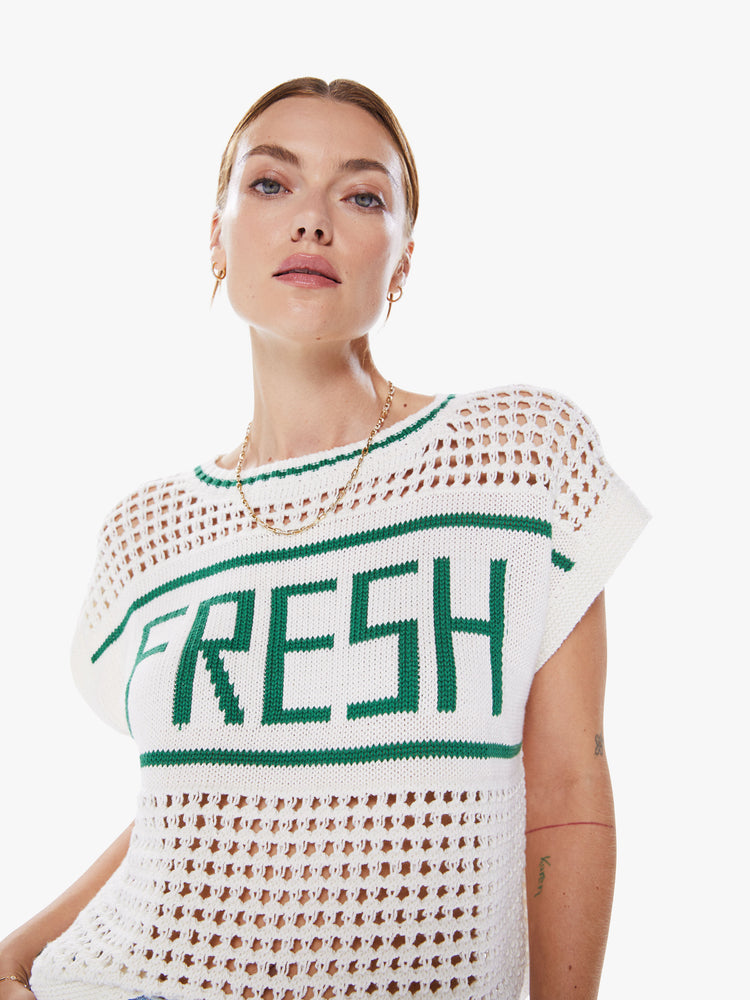 Close up view a crewneck top with boxy short sleeves and a loose fit in white with green detail with ribbed hems, a chest panel with text and an open-weave knit.