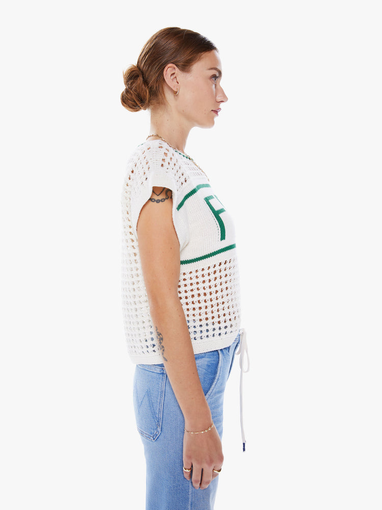 Side view a crewneck top with boxy short sleeves and a loose fit in white with green detail with ribbed hems, a chest panel with text and an open-weave knit.