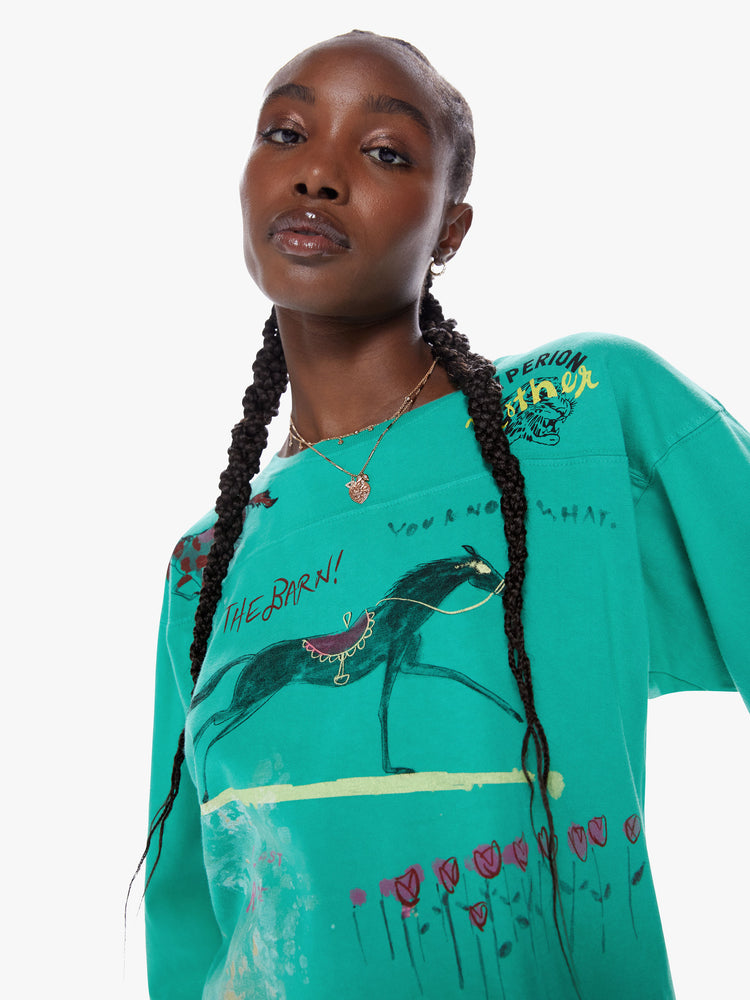 Close up view of woman football tee with a boat neck, 3/4 sleeves, drop shoulders and a boxy fit. Made from 100% cotton in a bright turquoise hue with a hand drawn horse graphic, scribbled text and a number on the back.