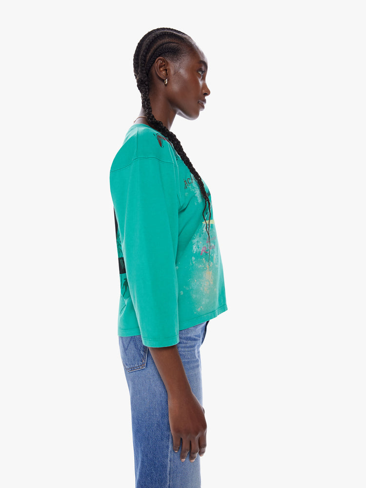 Side view of woman football tee with a boat neck, 3/4 sleeves, drop shoulders and a boxy fit. Made from 100% cotton in a bright turquoise hue with a hand drawn horse graphic, scribbled text and a number on the back.