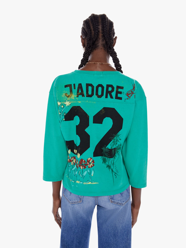 Back view of woman football tee with a boat neck, 3/4 sleeves, drop shoulders and a boxy fit. Made from 100% cotton in a bright turquoise hue with a hand drawn horse graphic, scribbled text and a number on the back.