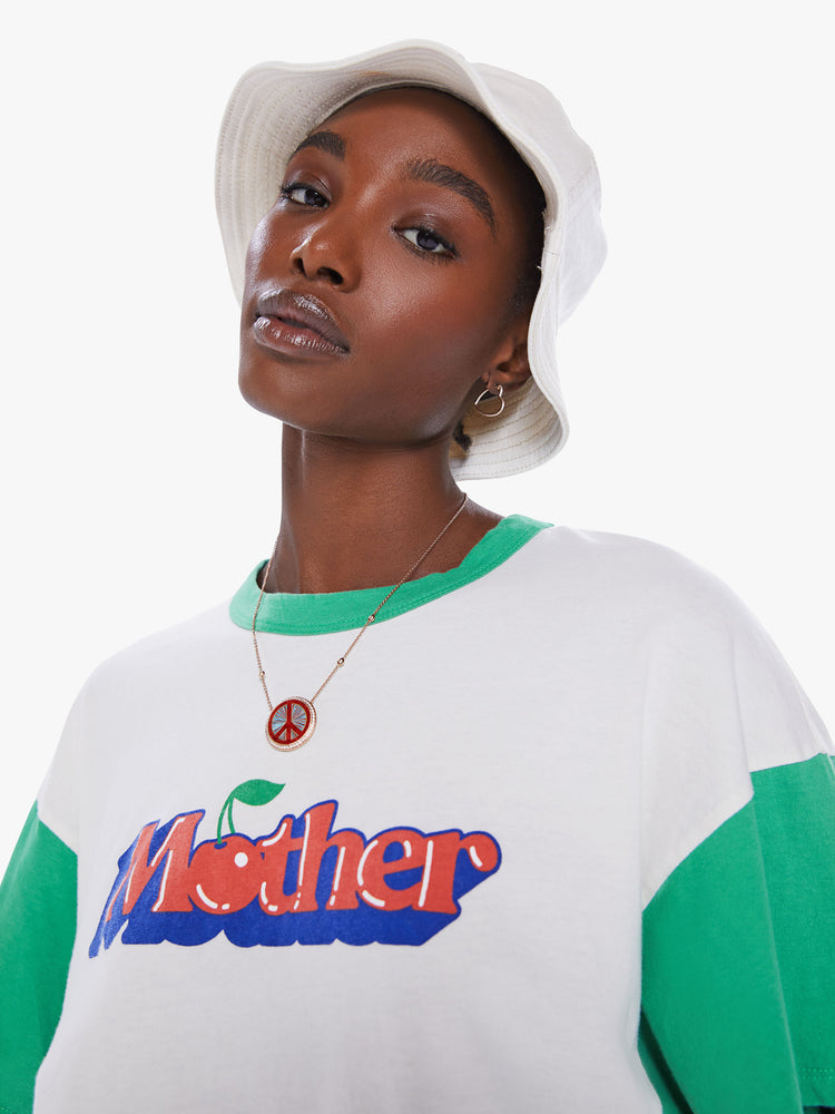 Close up view of woman oversized cropped tee with drop shoulders, subtle bat wings and a boxy fit in white with teal crewneck and sleeves with graphic in 3D text.