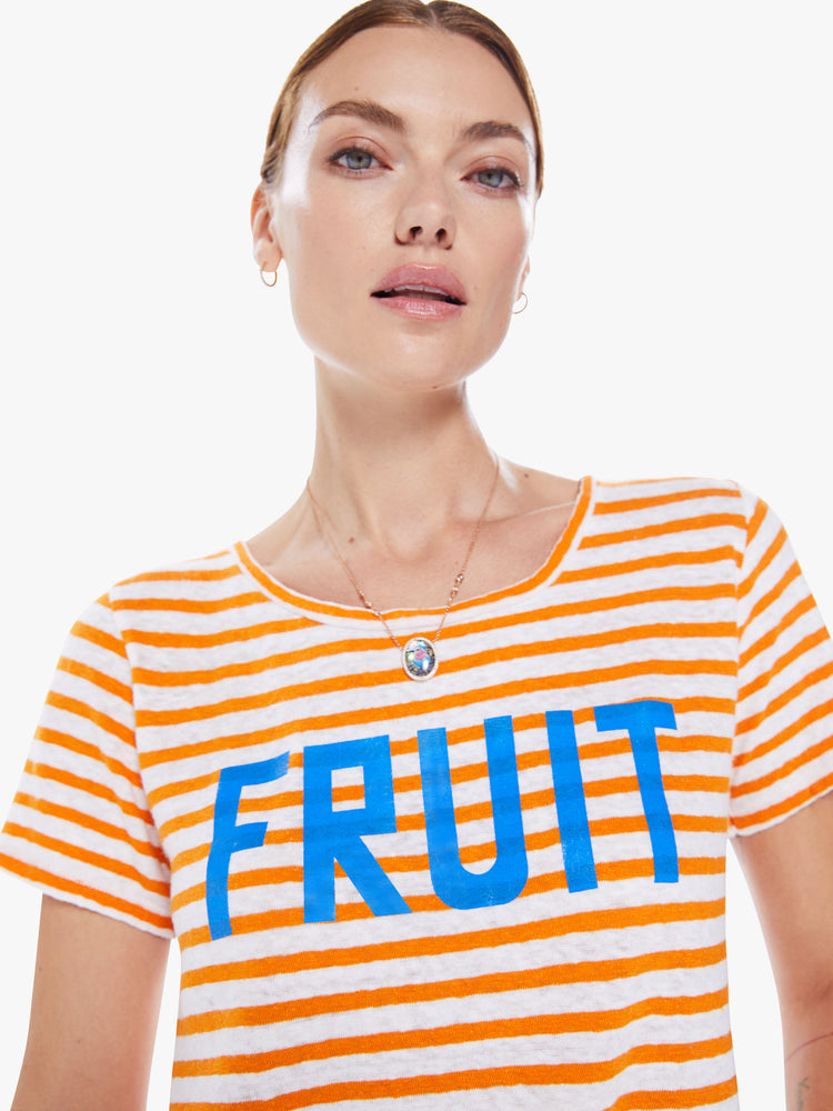 Close up view of a woman's boxy crewneck with short sleeves and a cropped hem in orange stripes and bright blue text.