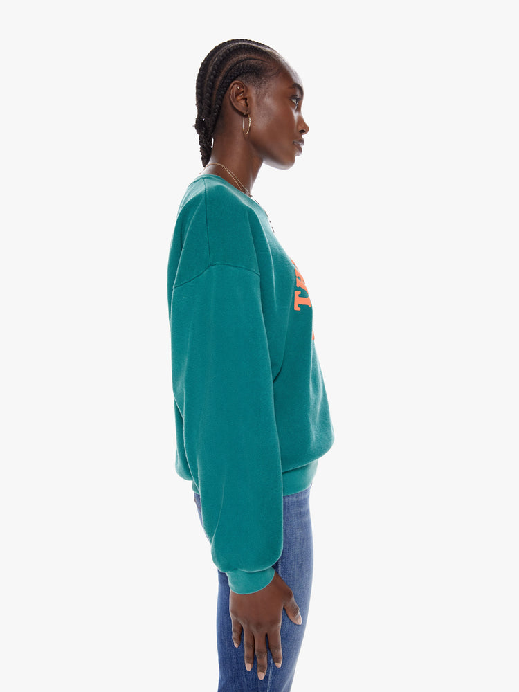 Side view of a woman in a crewneck sweatshirt with dropped sleeves, a relaxed fit in a dark turquoise hue that features puff-ink text that reads The Whole Wide World